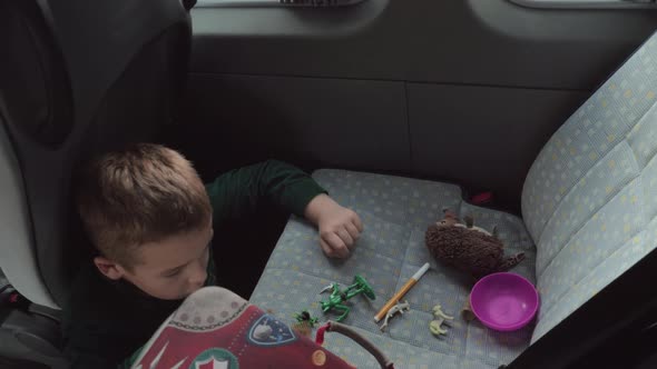 A boy sitting on a cars floor playing with some toys on a back seat