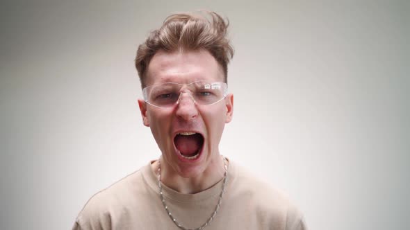 Funny Angry Man in Glasses Looks at the Camera and Screams on a White Background
