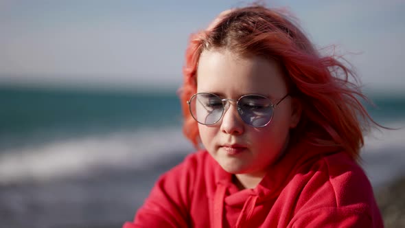 Little Girl with Pink Hair is Sitting on Seashore Cute Child on Beach in Spring Windy Day