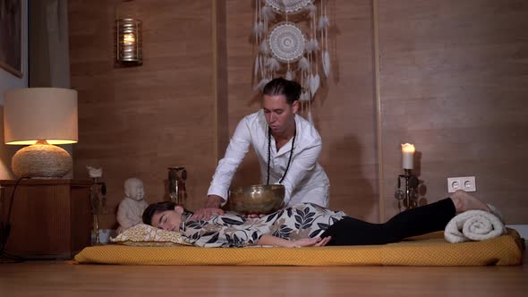 Zen master playing bowl gong above relaxed woman during meditation