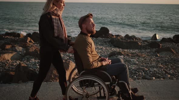 Woman Taking Care of Disabled Husband and Walking with Him By the Sea