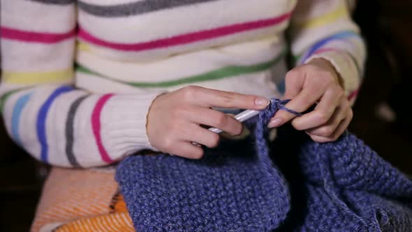 A Young Girl Knits a Scarf Snood Sitting on the Couch Covered with a Blanket