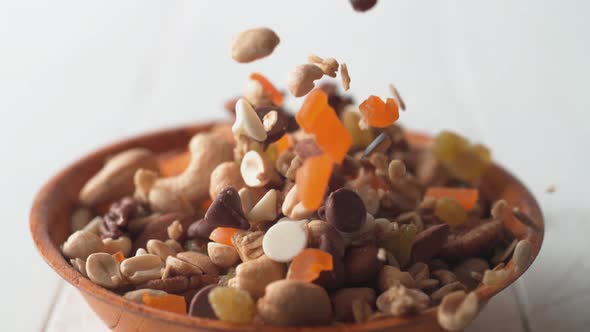 Camera follows trail mix nuts and dried fruits falling into a bowl. Slow Motion.