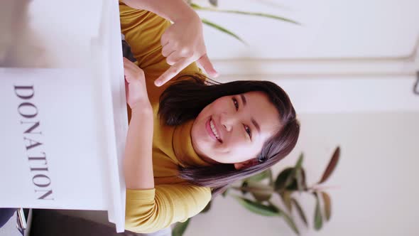 Young Asian woman pointing at box with donations. Upright video about donation.