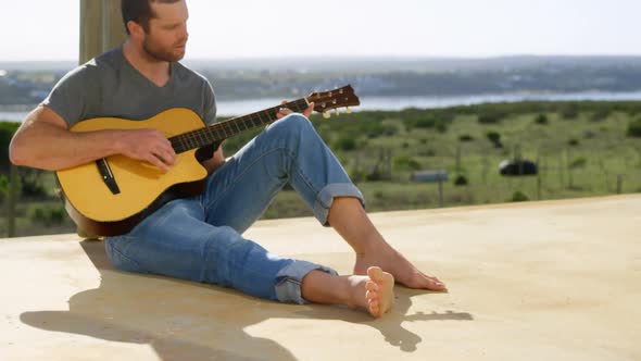 Front view of caucasian man playing guitar at porch of beach house 4k