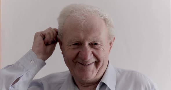 Joyful Senior Man Combs His Gray Hair and Laughs at the Camera on the Background