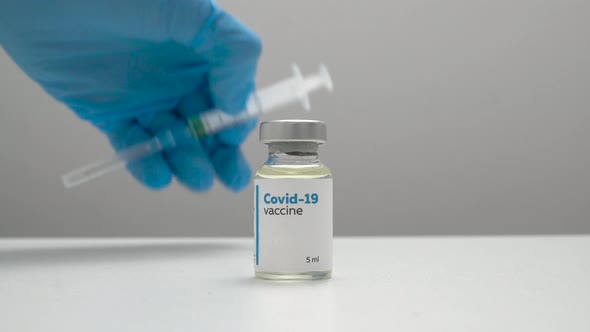 Doctor's hands in blue medical gloves taking a dose of coronavirus vaccine in a glass bottle