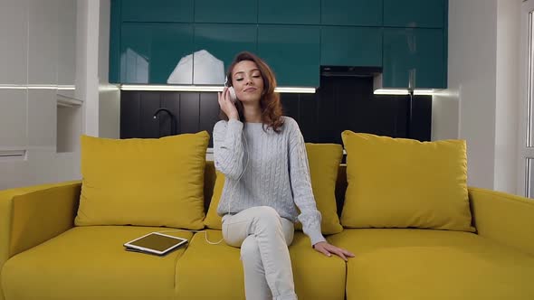 Girl Relaxing Under Music in Her Earphones Sitting on the Cozy Kitchen Couch