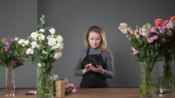 Blonde Florist Woman Uses Mobile Phone in Floristry Workshop