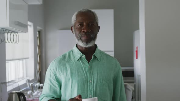 A senior african american man smiling at the camera and drinking a beverage social distancing in qua