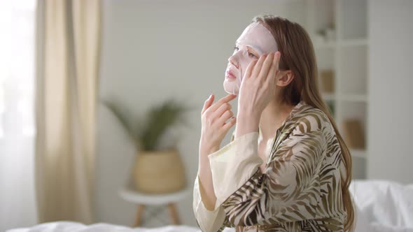 Young Woman Putting on Face Mask in Morning