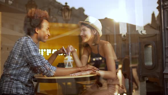 Two Beautiful Girls Smiling Speaking Holding Hands Resting in Cafe Slow Motion