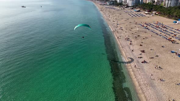 Aerial drone view of parachute jumper flying over beautiful beach