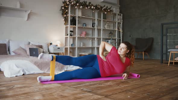 Young Overweight Woman Doing Legs Exercises with Elastic Band on Floor at Home