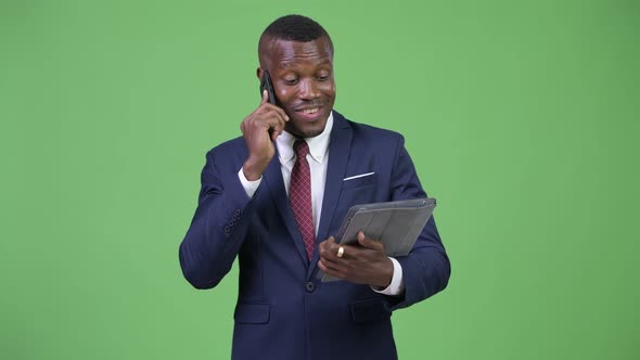 Young Happy African Businessman Talking on the Phone While Using Digital Tablet