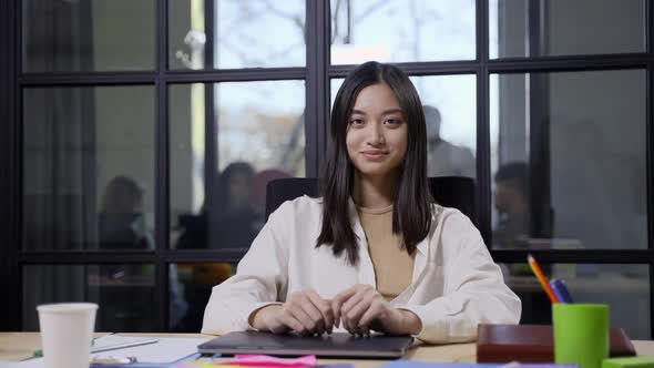 Smiling Asian Female Posing on Camera at Workplace