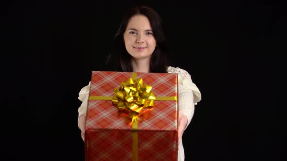 Young Woman Gives a Gift Box on Black Background. Gift Box with White Ribbon for Happy New Year