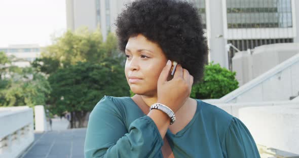 Happy plus size biracial woman using smartphone and wearing earphones in city