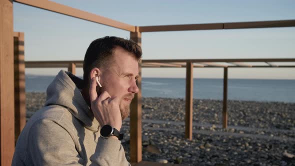 Man Is Checking His Handsfree Set in His Ear Sitting on Sea Shore
