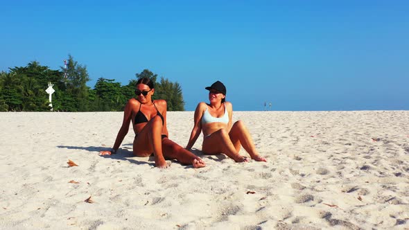 Pretty smiling girls relaxing in the sun at the beach on sunny blue and white sand background 