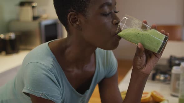 Portrait of smiling african american attractive woman drinking homemade smoothie in kitchen