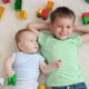Smiling Baby Boy with Older Brother Lying on Carpet Next to Heap of Colroful Toys and Looking Up in - VideoHive Item for Sale