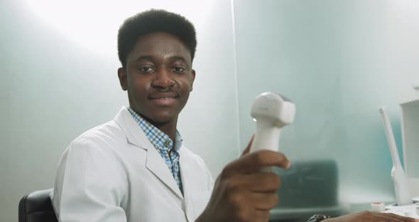 Smiling African Man Doctor with Ultrasound Transducer in Hand Working on Modern