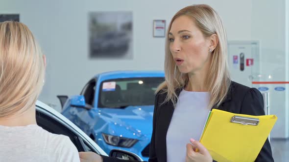 Mature Saleswoman Talking To Her Client, Working at Cars Dealership Salon
