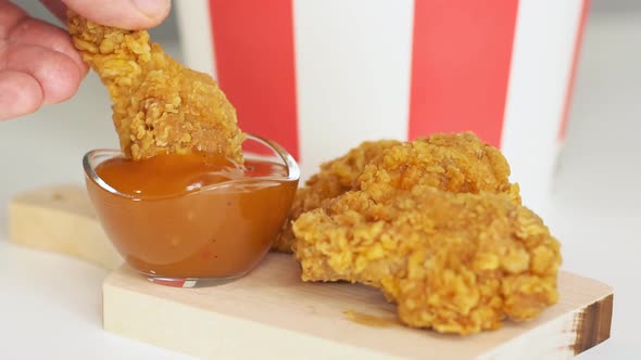 Man dunks fried chicken wing in sauce. Close-up. Slow motion.