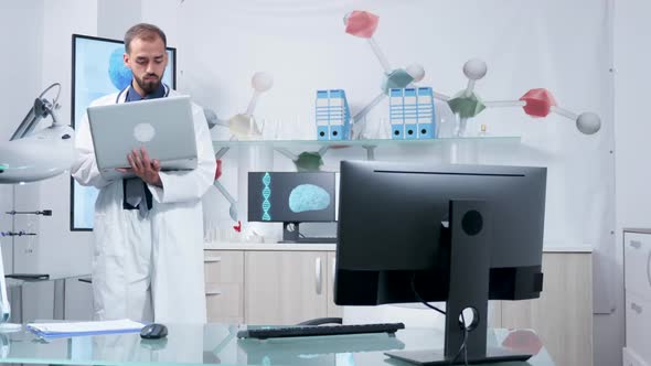 Doctor in His Modern Office Standing and Typing at His Laptop