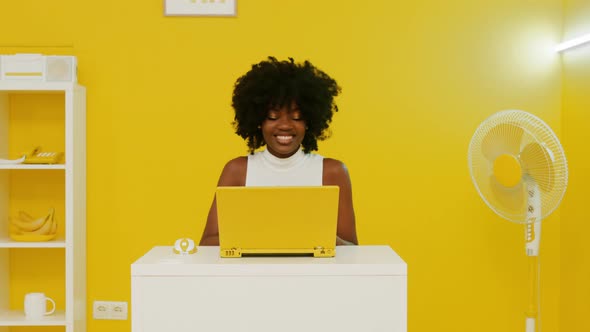 Happy Black Woman Is Using Laptop In Yellow Room
