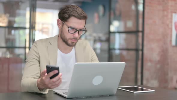 Young Man with Laptop Using Smartphone