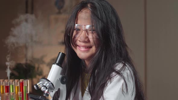 Young Scientist Girl With Dirty Face Looking At Microscope And Smiles To Camera In Laboratory