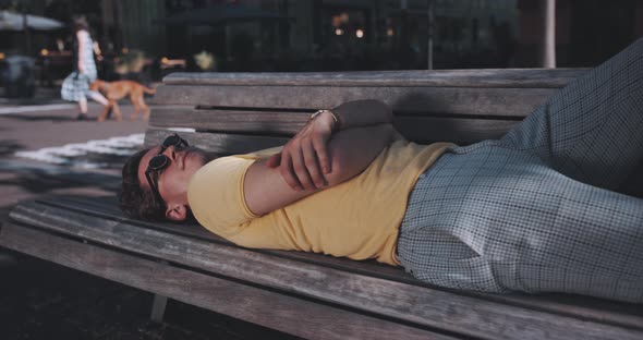 Man lays on sunny park bench