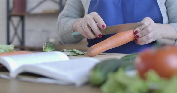 Middle-aged Female Caucasian Hand Peeling Carrot with Knife. Close-up of Senior Unrecognizable
