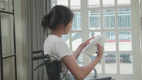 Asian Woman Sitting In A Wheelchair Reading Book Near Door In The House