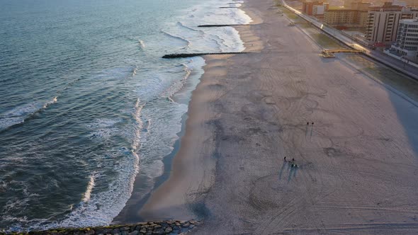 A high angle shot over an empty beach during sunset. The drone camera hovers up high then booms down