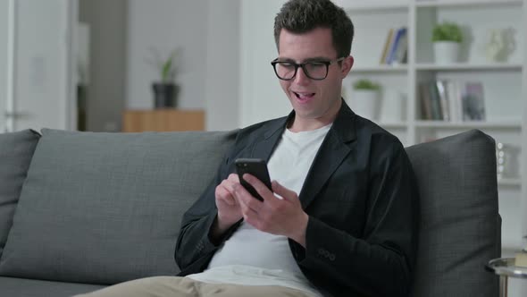 Excited Young Male Designer Celebrating Success on Smartphone 