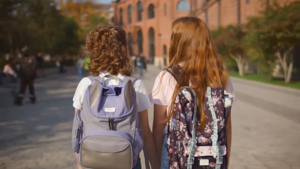 Back View of Two Preteen Girls with Backpack Holding Hands Going To School Together