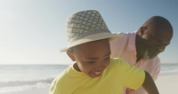 Smiling senior african american man with grandson playing on sunny beach