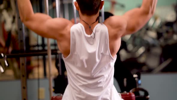 Rear extreme closeup of young bodybuilder doing lat pulldowns on a machine.