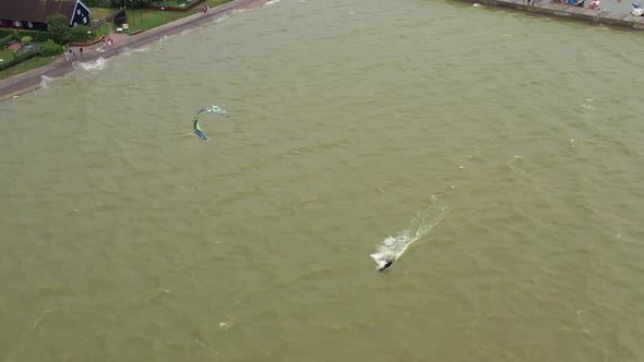 AERIAL: Follow Shot of Isolated Kiteboarder Who Swims Past Stone Pier on a Cloudy Day