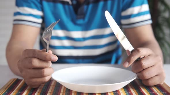 Hand Holding Cutlery with Empty Plate on Wooden Table