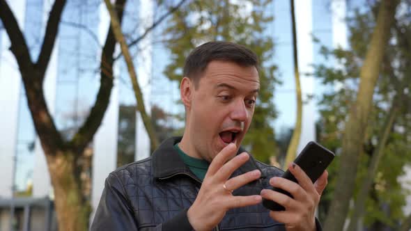 Excited Guy Looks at Phone and Celebrates Big Win Financial Good News Success Achievement Cell Phone