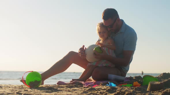 Father and Baby Daughter Eating Apple on Beach