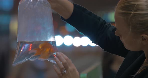 Woman holds in hand plastic package with aquarium gold fish in the shopping mall Hong Kong, China