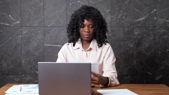 Black Businesswoman Gathers Papers and Types on Laptop