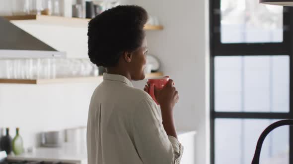 Happy african american woman drinking coffee in kitchen