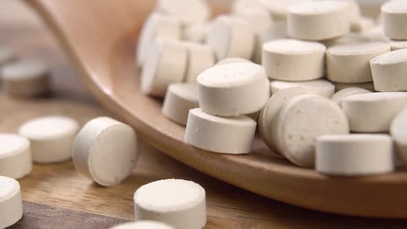 Herbal round food supplement tablets. Falling pills into a wooden spoon in slow motion