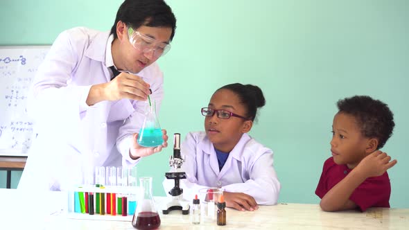 Young Scientist Holding a Flask and Teaching Two African American Kids in Chemistry Lab Experiment